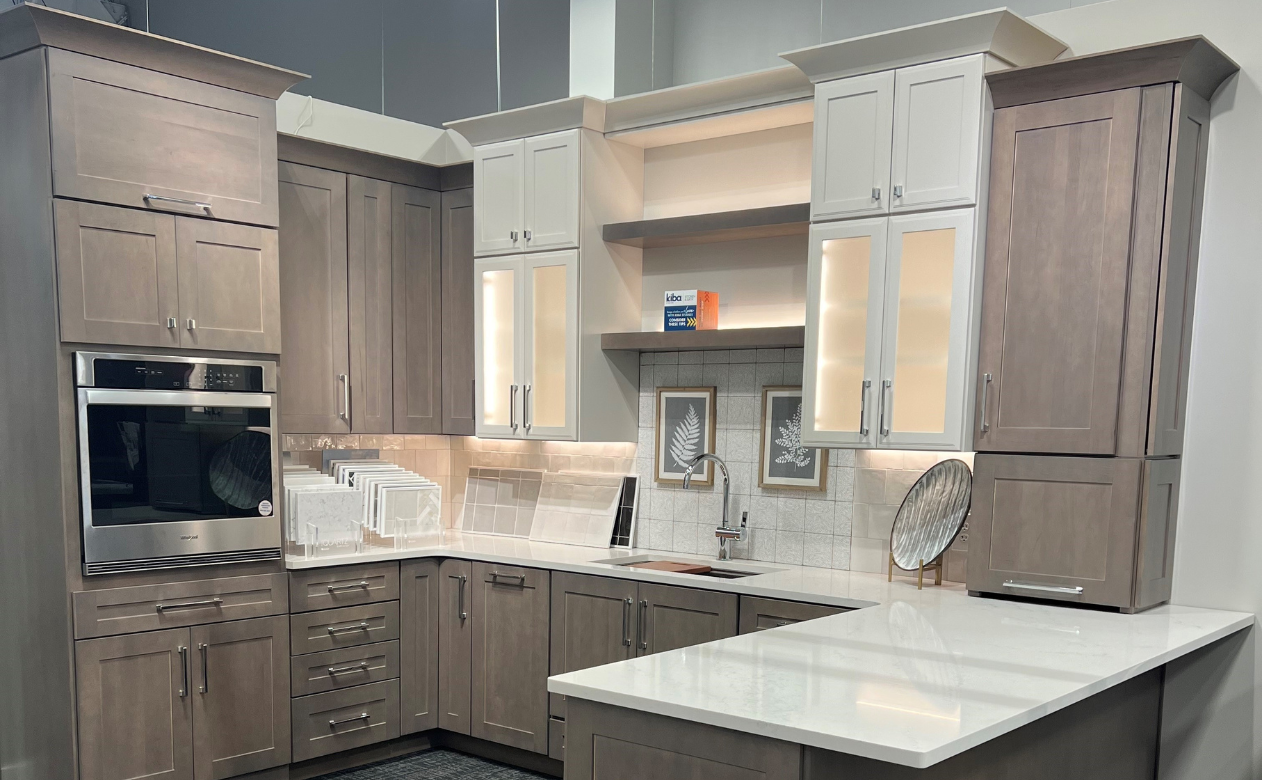 Modern kitchen with greige and white cabinets, built-in oven, light countertops, and tiled backsplash